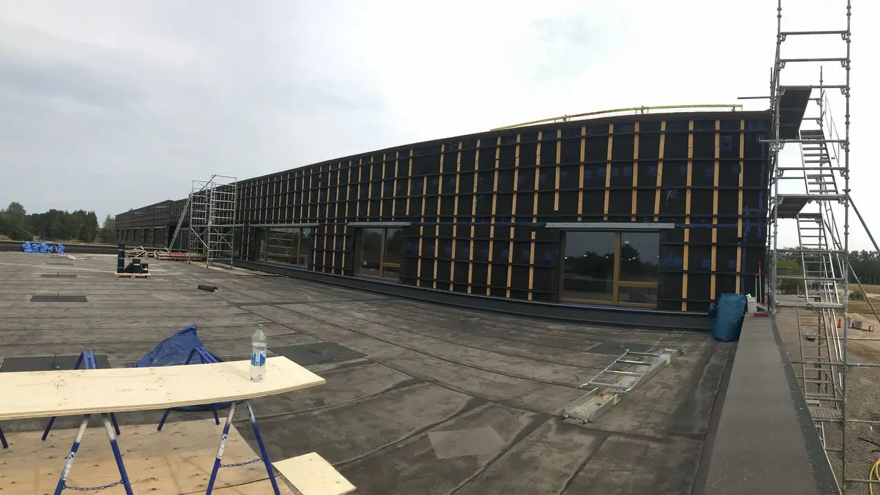 Panorama över en lång skolfasad med byggställning under isolering